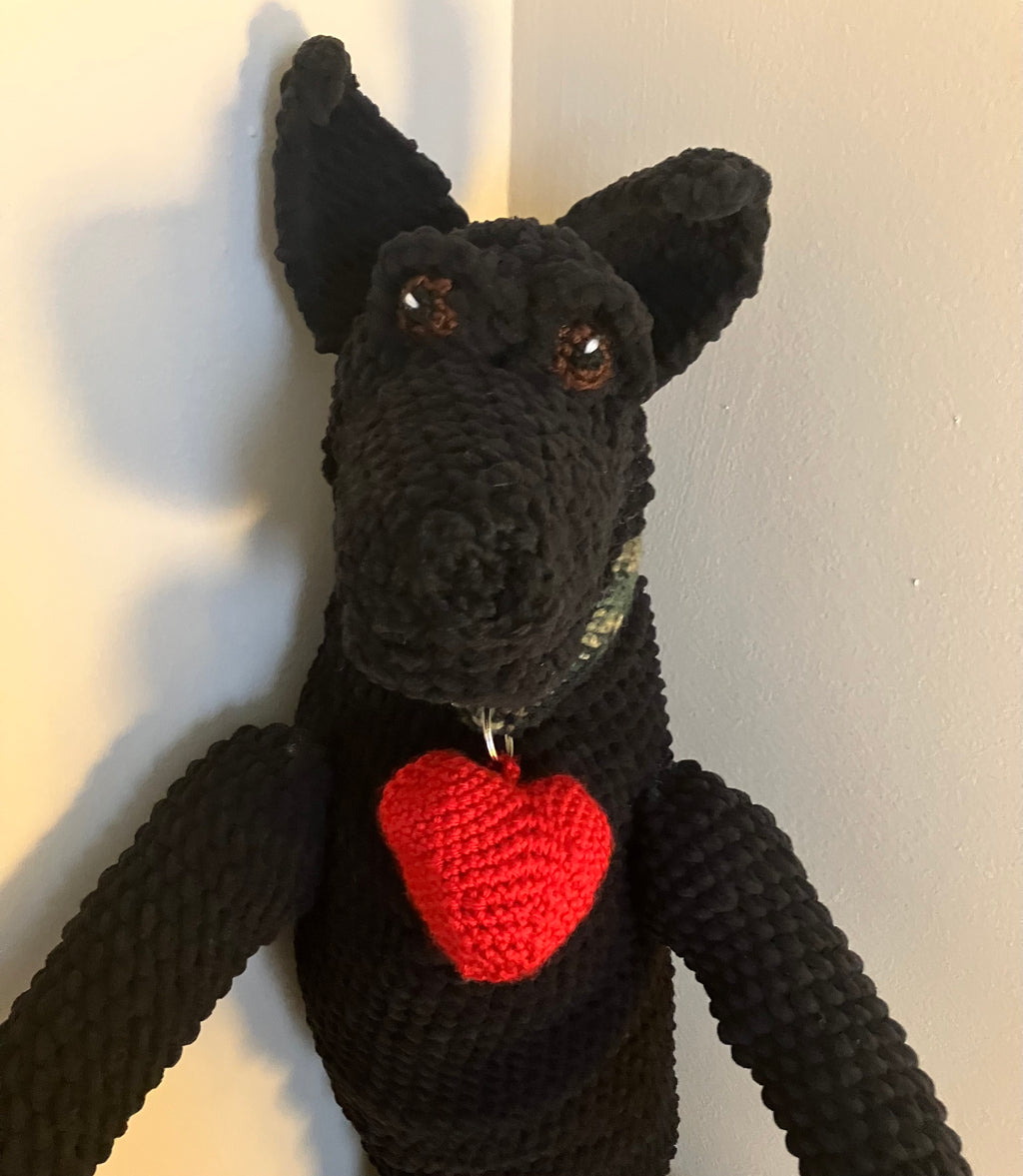 Black crochet dog toy with a red heart on a white background